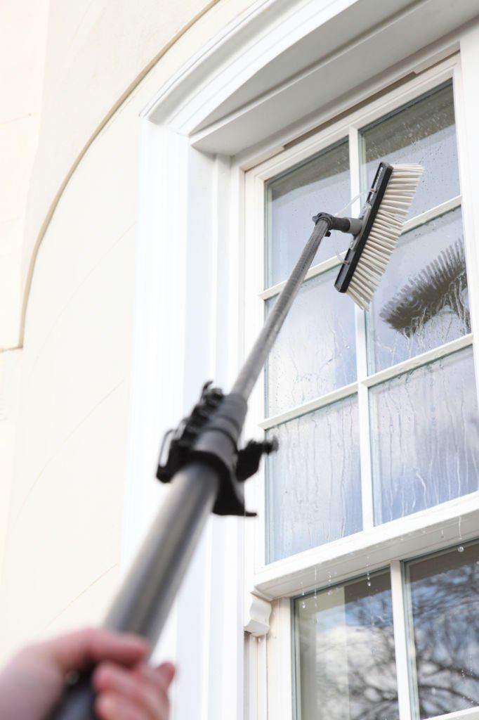 Window cleaner using a long-handled brush to clean a window