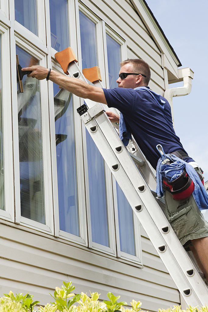 Window cleaner on a ladder cleaning an upstairs window